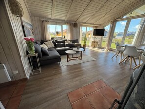A modern living room with a sectional sofa, a round coffee table, and a dining area with a table and chairs. - North Sea vacation home Huus Eiderente - relaxation, wellness, fireplace, fiber optic WLAN (Wesselburenerkoog)