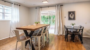 Un coin repas avec une table et des chaises en bois, une fenêtre avec des rideaux et une plante accrochée au mur.