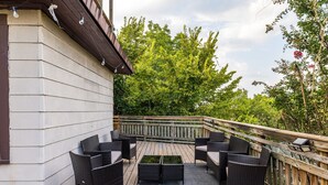 A wooden deck with wicker furniture and a small table, surrounded by a wooden railing and greenery.