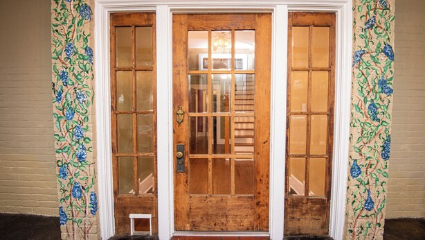 A wooden double door with glass panels, flanked by decorative floral wall panels.