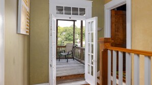 A wooden deck with a chair, a white door leading outside, and a view of greenery.