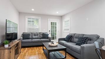 A modern living room with two grey sofas, a wooden coffee table, and a TV on a wooden cabinet.