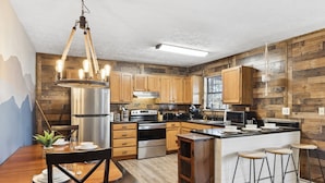 A modern kitchen with wooden cabinets, stainless steel appliances, and a bar area with stools.