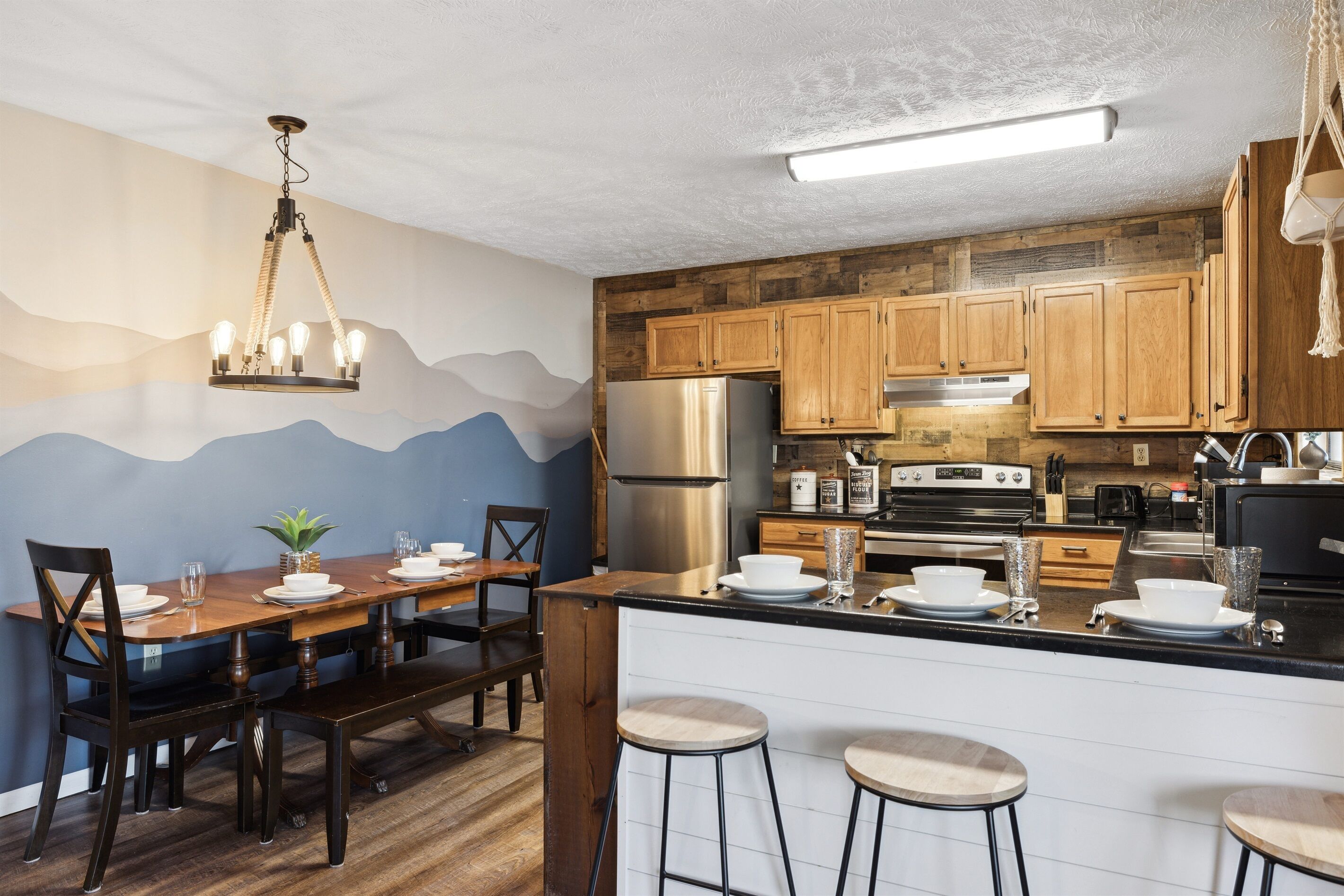 A modern kitchen with wooden cabinets, a stainless steel refrigerator, and a bar area with stools.