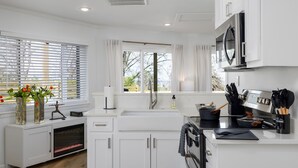 A modern kitchen with white cabinetry, a built-in oven, a microwave, and a window with blinds. - The Hobbit House - City Views/Deck & Patio/Firepit (birmingham)