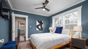 Un dormitorio con cama, mesitas de noche, ventilador de techo y ventana con persianas.