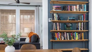 Una sala de estar moderna con una estantería llena de libros, un sofá y una mesa de comedor con sillas.