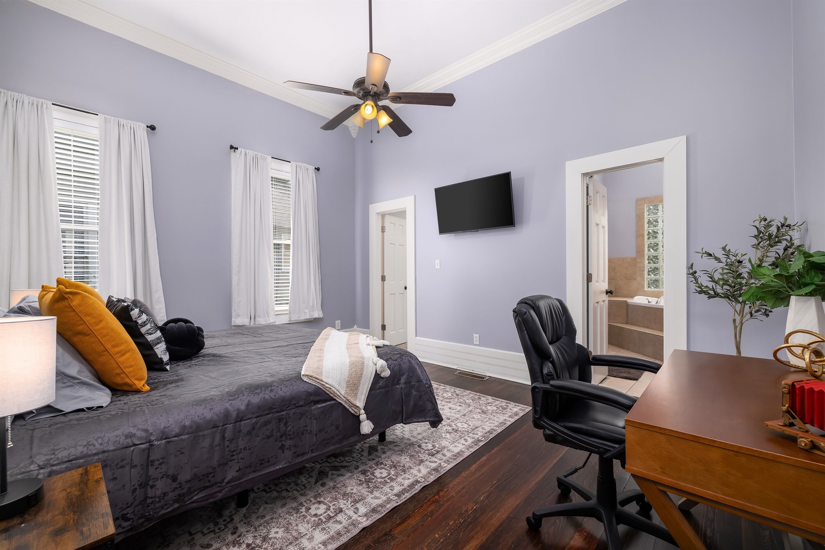 A bedroom with a bed, a desk, a chair, a TV, and a ceiling fan.