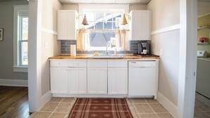A compact kitchen with white cabinets, a wooden countertop, a coffee maker, and a window with curtains.