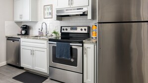 Une cuisine moderne avec des meubles blancs, des appareils en acier inoxydable, une machine à café et un égouttoir à vaisselle.