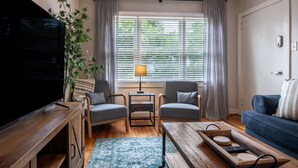 Un salon avec un téléviseur, deux fauteuils, une table basse et un canapé.