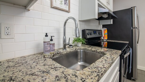 Una cocina con encimera de granito, pileta de acero inoxidable y refrigerador negro.