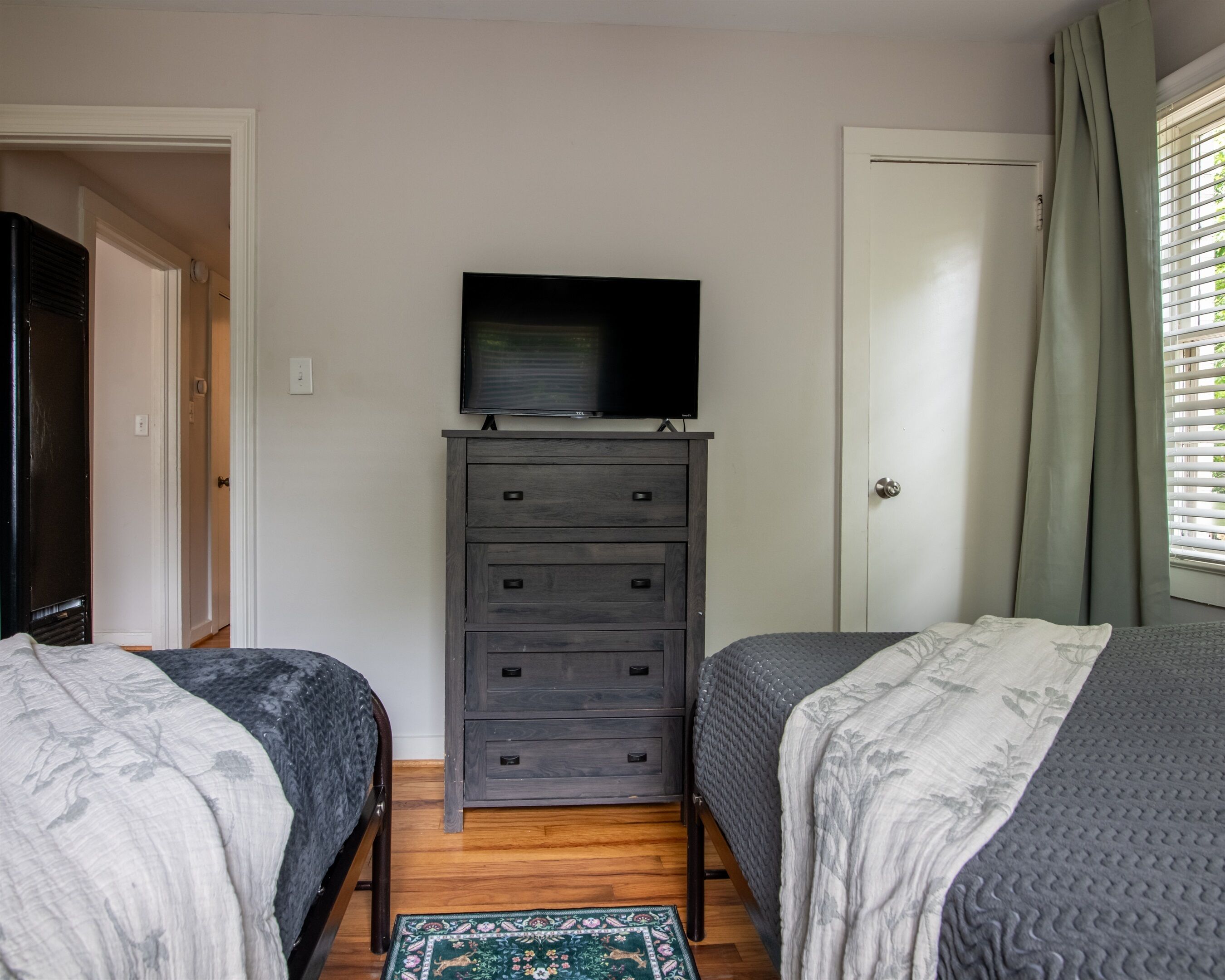 A bedroom with two beds, a dresser, a television, and a window with curtains.