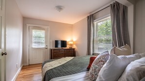 Un dormitorio con cama, cómoda, televisor y ventana con cortinas.