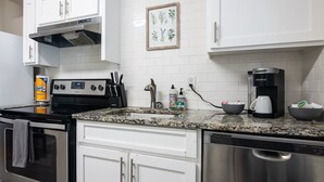 A modern kitchen with white cabinets, a stainless steel dishwasher, a coffee maker, and a stove.