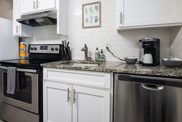 A modern kitchen with white cabinets, a stainless steel dishwasher, a coffee maker, and a stove.