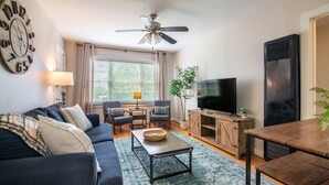 A living room with a sofa, chairs, a coffee table, a TV, and a ceiling fan.