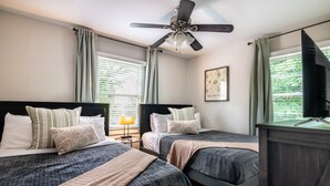 A bedroom with two beds, a ceiling fan, a TV, and a window with curtains.