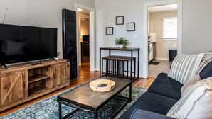 A living room with a TV, wooden entertainment unit, a coffee table, a sofa, and a small table with a plant.