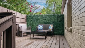 A wooden deck with wicker furniture and a green hedge wall.