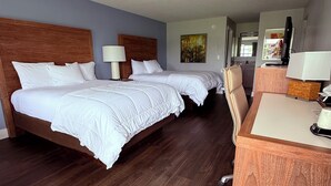 Habitación de hotel con dos camas, un escritorio, una silla, una lámpara y un cuadro en la pared.