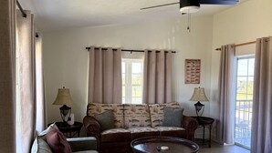 Una sala de estar con ventilador de techo, un sofá, una mesa de centro y un tapete estampado.