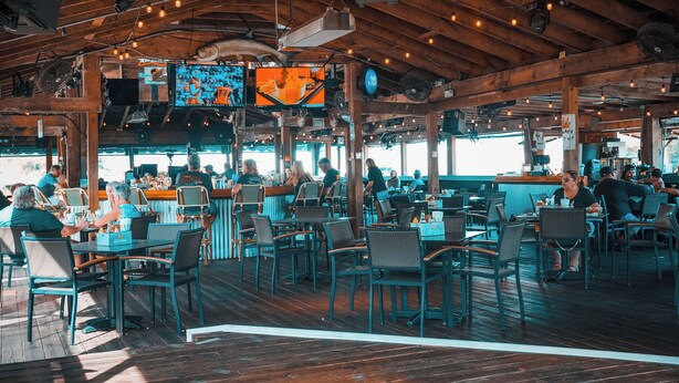 Un restaurante con vigas de madera, luces colgantes, mesas y sillas, y una zona de bar.