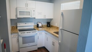 Una cocina compacta con armarios blancos, un microondas integrado, una estufa y un refrigerador.