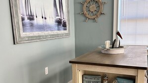 A room with a wooden table displaying various signs, a sailboat painting, and a ship's wheel decoration. - Cozy Cottage At Lake Weir (Ocklawaha)