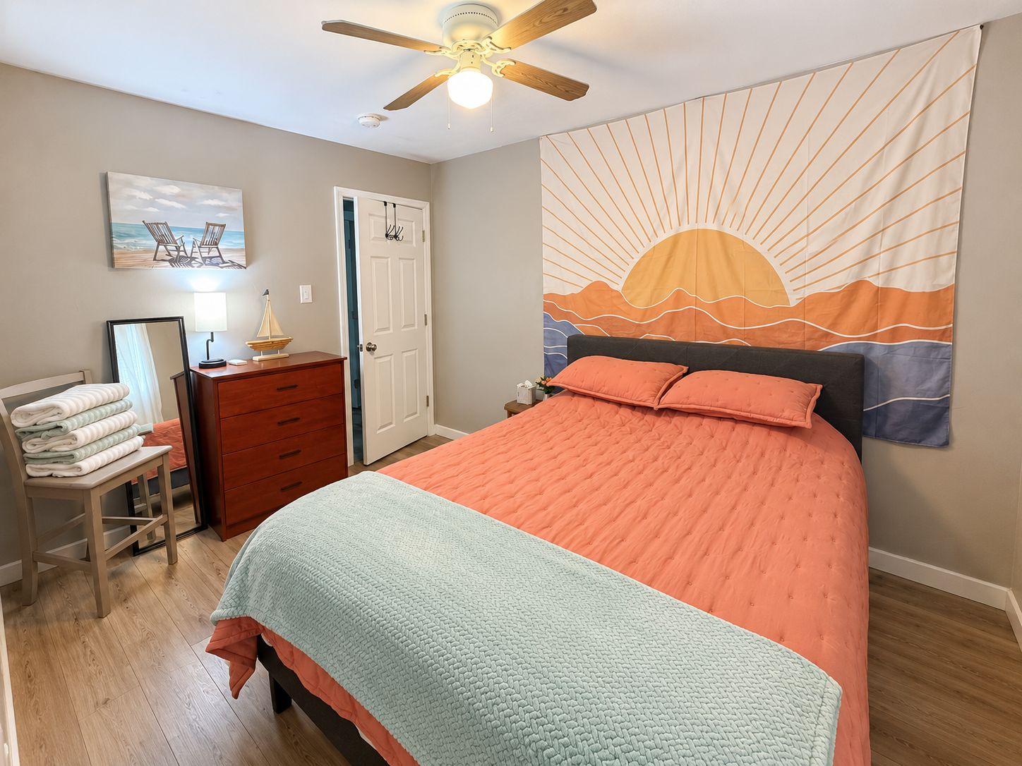 A bedroom with a bed, a dresser, a mirror, a ceiling fan, and a tapestry.