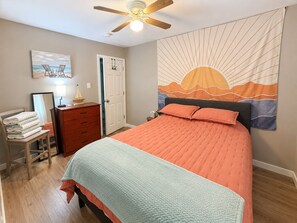 A bedroom with a bed, a dresser, a mirror, a ceiling fan, and a tapestry.
