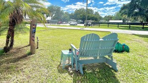Une zone herbeuse avec une clôture en bois, un palmier et une chaise Adirondack bleue.