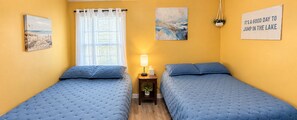 A room with two beds, a window with sheer curtains, a bedside lamp, and a motivational poster.