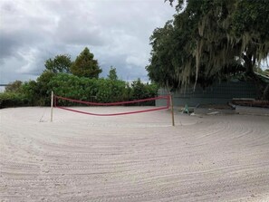 Ein Sandvolleyballfeld mit rotem Netz, umgeben von Bäumen und einem Gebäude im Hintergrund.