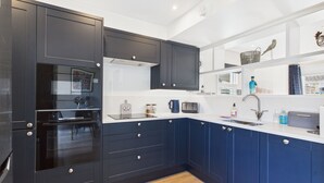 A modern kitchen with dark blue cabinets, white countertops, and a built-in oven. - Charming 2-bed Family Cottage Your West Bay Retreat (Yarmouth)