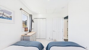 A bedroom with two beds, a desk, a window with a view, and a door leading to another room. - Charming 2-bed Family Cottage Your West Bay Retreat (Yarmouth)