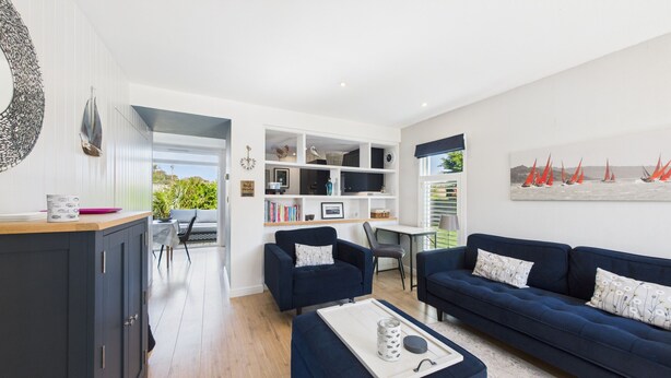 A modern living room with a dark blue sofa, a dining area with a table and chairs, and a kitchen area with cabinets and a countertop. - Charming 2-bed Family Cottage Your West Bay Retreat (Yarmouth)