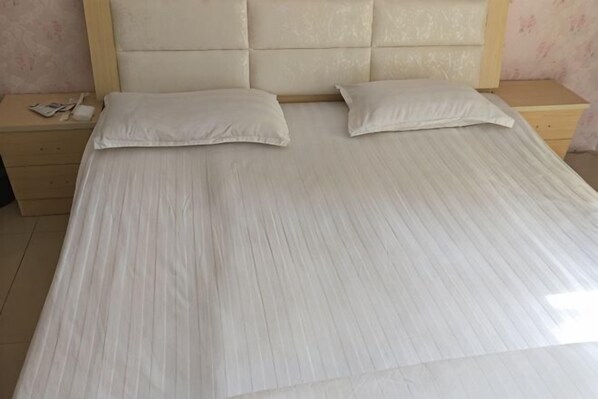 A bed with two pillows, a wooden headboard, and a nightstand with a phone and a book.