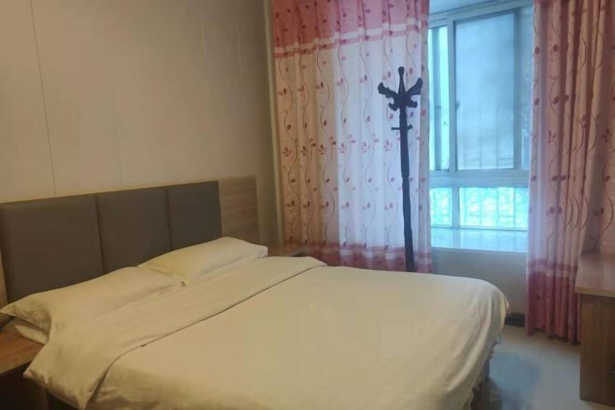 Un dormitorio con cama, ventana con cortinas y cabecero de madera.