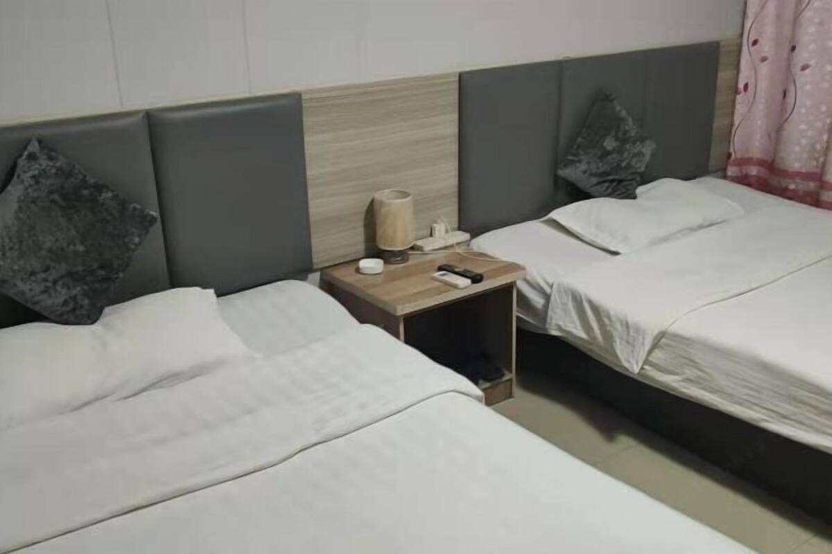 Habitación de hotel con dos camas, una mesita de noche con lámpara, control remoto y caja de pañuelos.