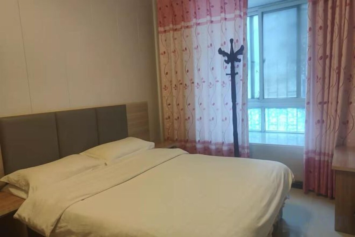 A bedroom with a bed, a window with curtains, and a coat rack.