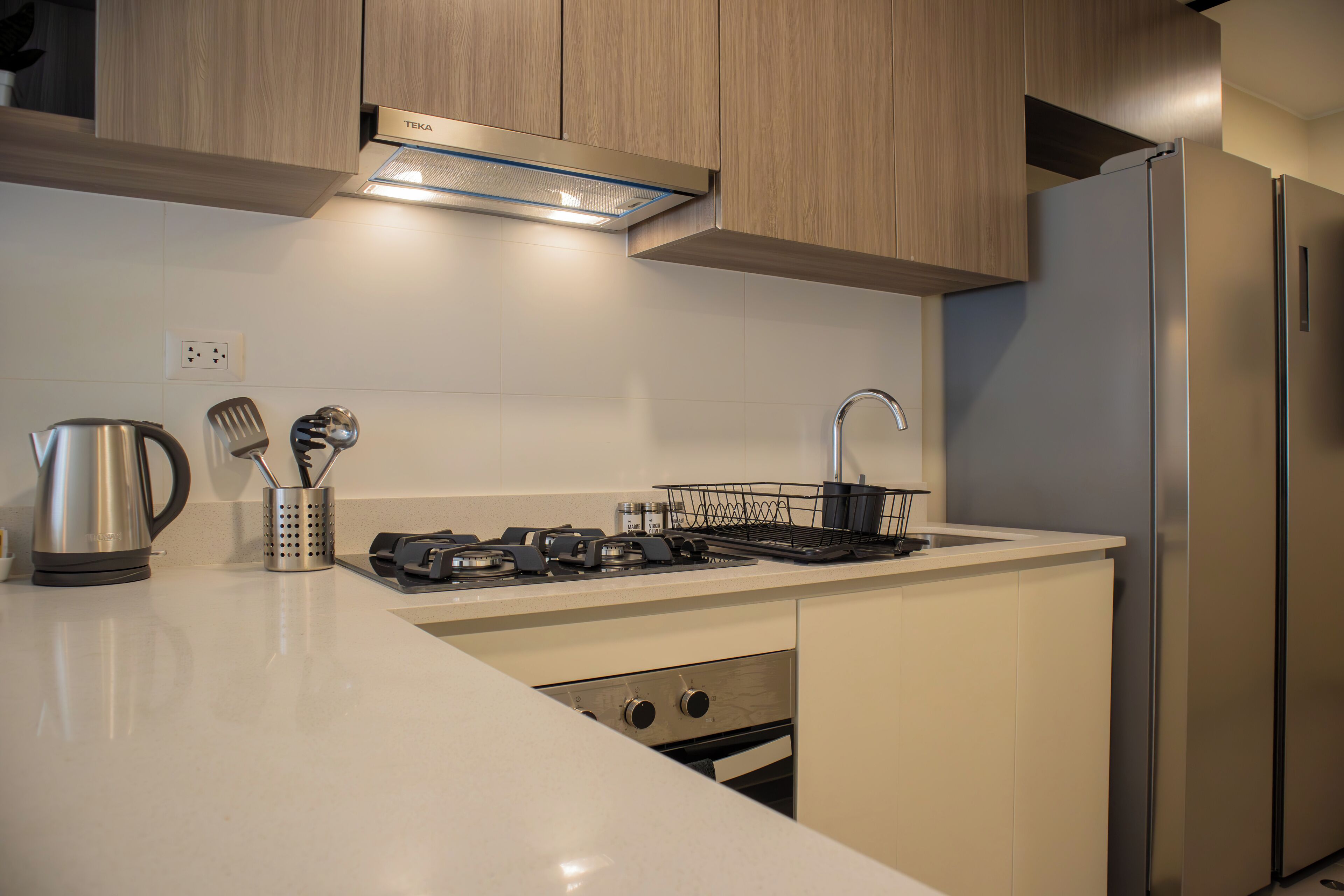 A modern kitchen with a stainless steel refrigerator, a built-in oven, and a gas stove.