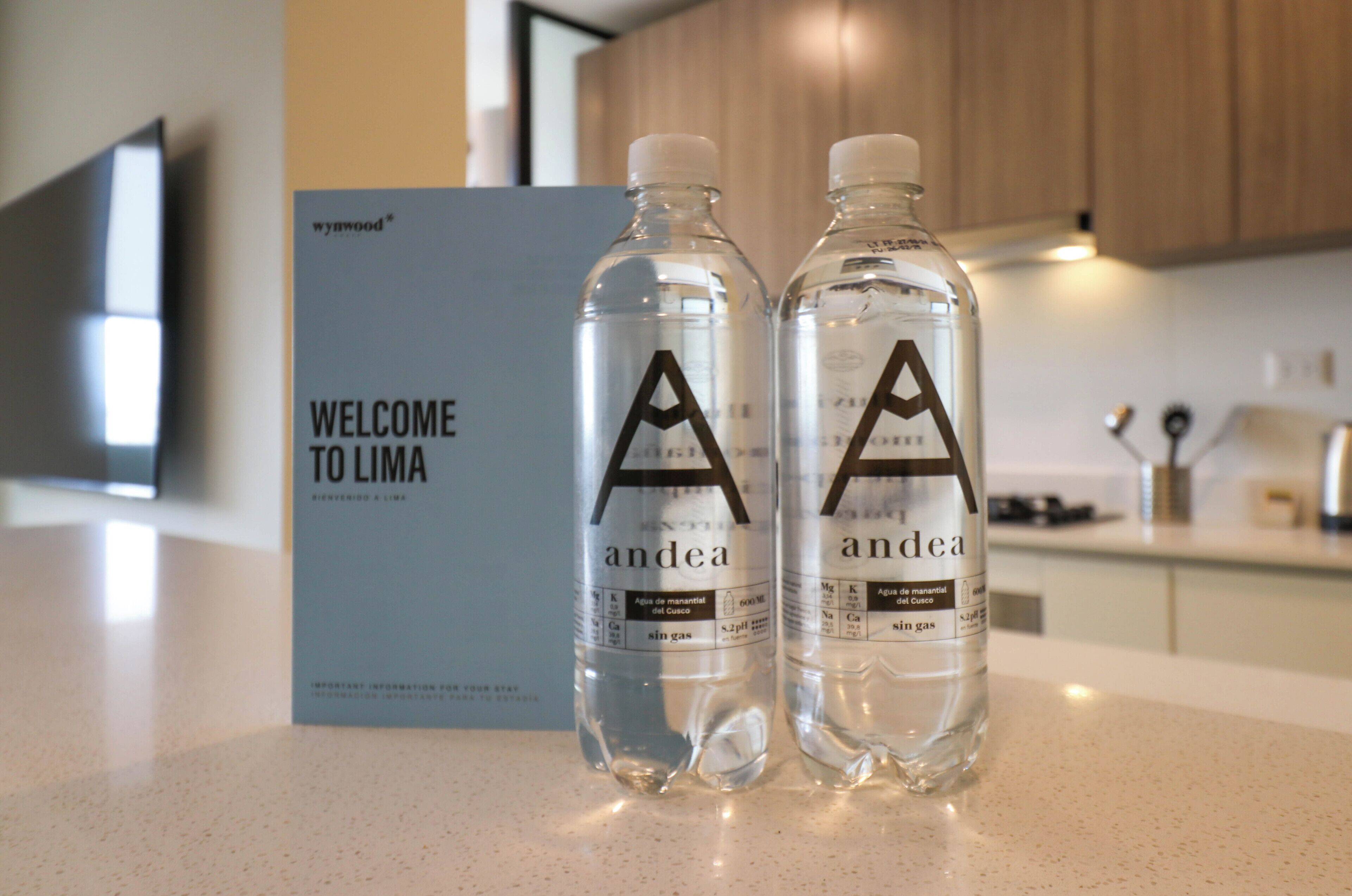 Two bottles of water labeled 'andea' on a kitchen counter with a 'WELCOME TO LIMA' sign in the background.