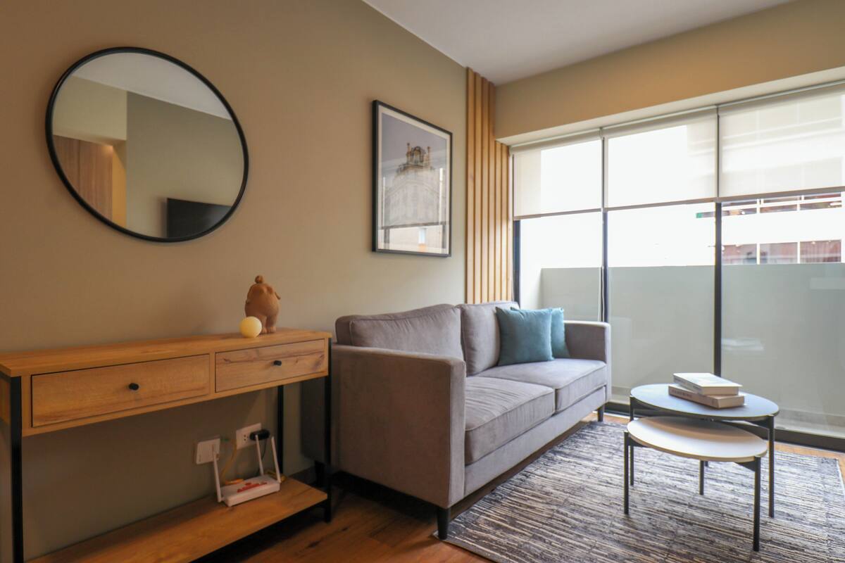 Un salon moderne avec un canapé, une petite table, un miroir et un tableau encadré accroché au mur.