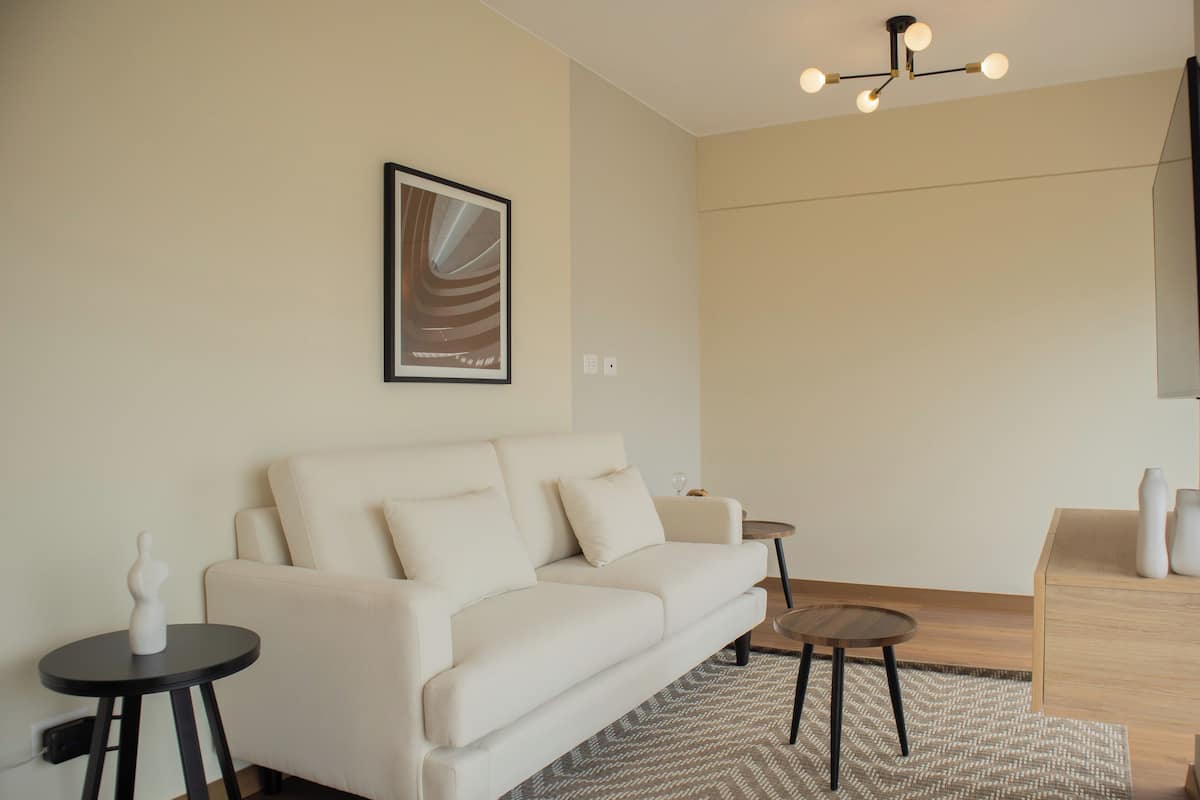 Un salon moderne avec un canapé blanc, une petite table ronde et une œuvre d’art abstraite encadrée accrochée au mur.