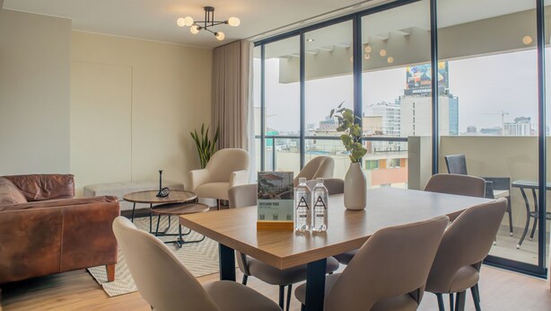 A modern hotel room with a large window, a dining area, a sofa, and a coffee table. - Treehouse by Wynwood House (Lima)