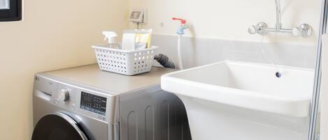 Un lavadero pequeño con lavadora de carga frontal, un lavabo y un centro de planchado a vapor.