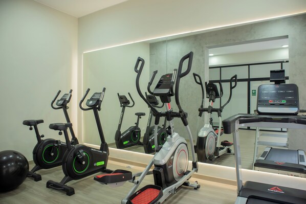 A gym with stationary bikes, treadmills, and a mirrored wall.
