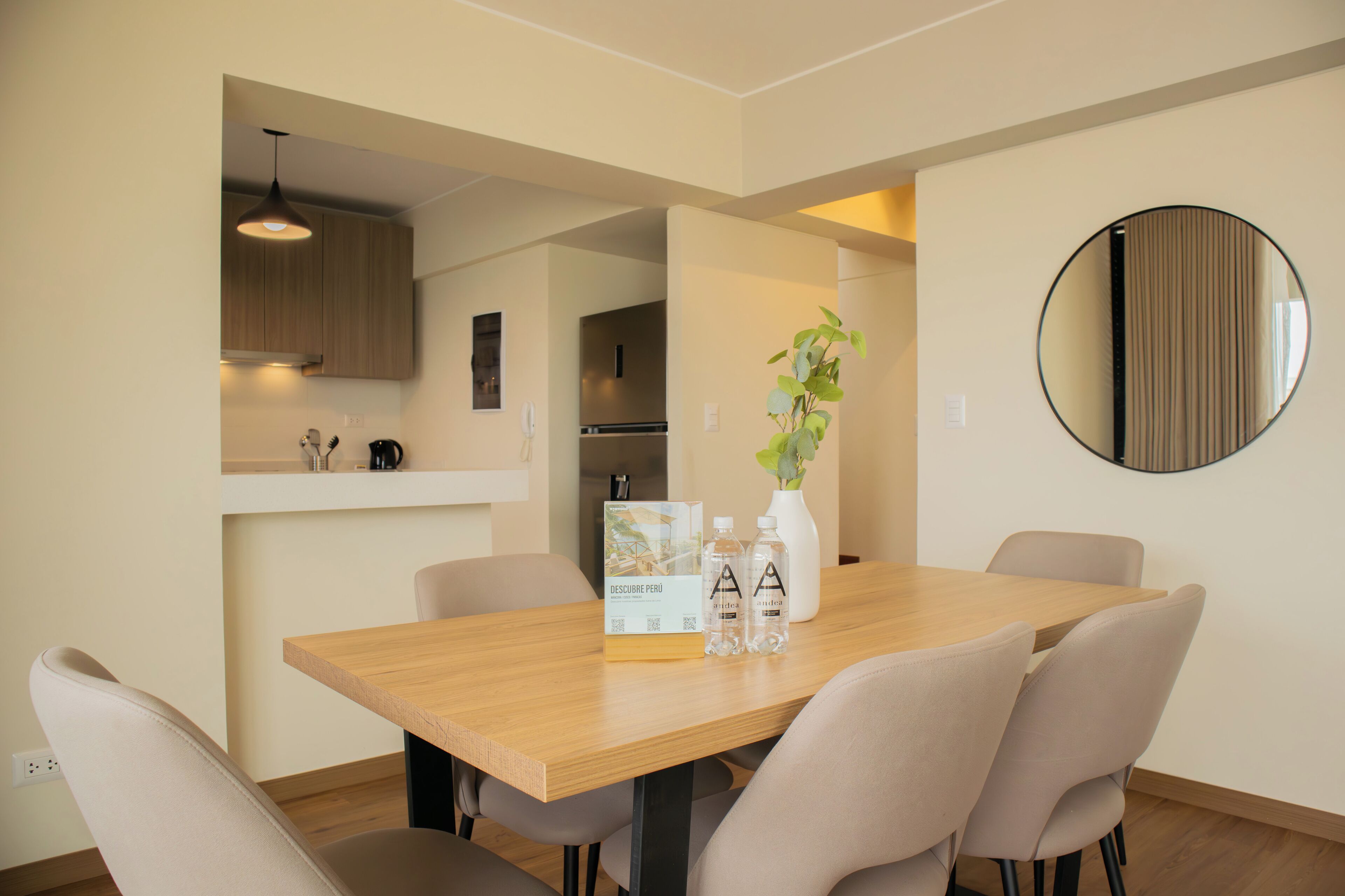 A dining area with a wooden table, four chairs, a vase with a plant, and two water bottles.