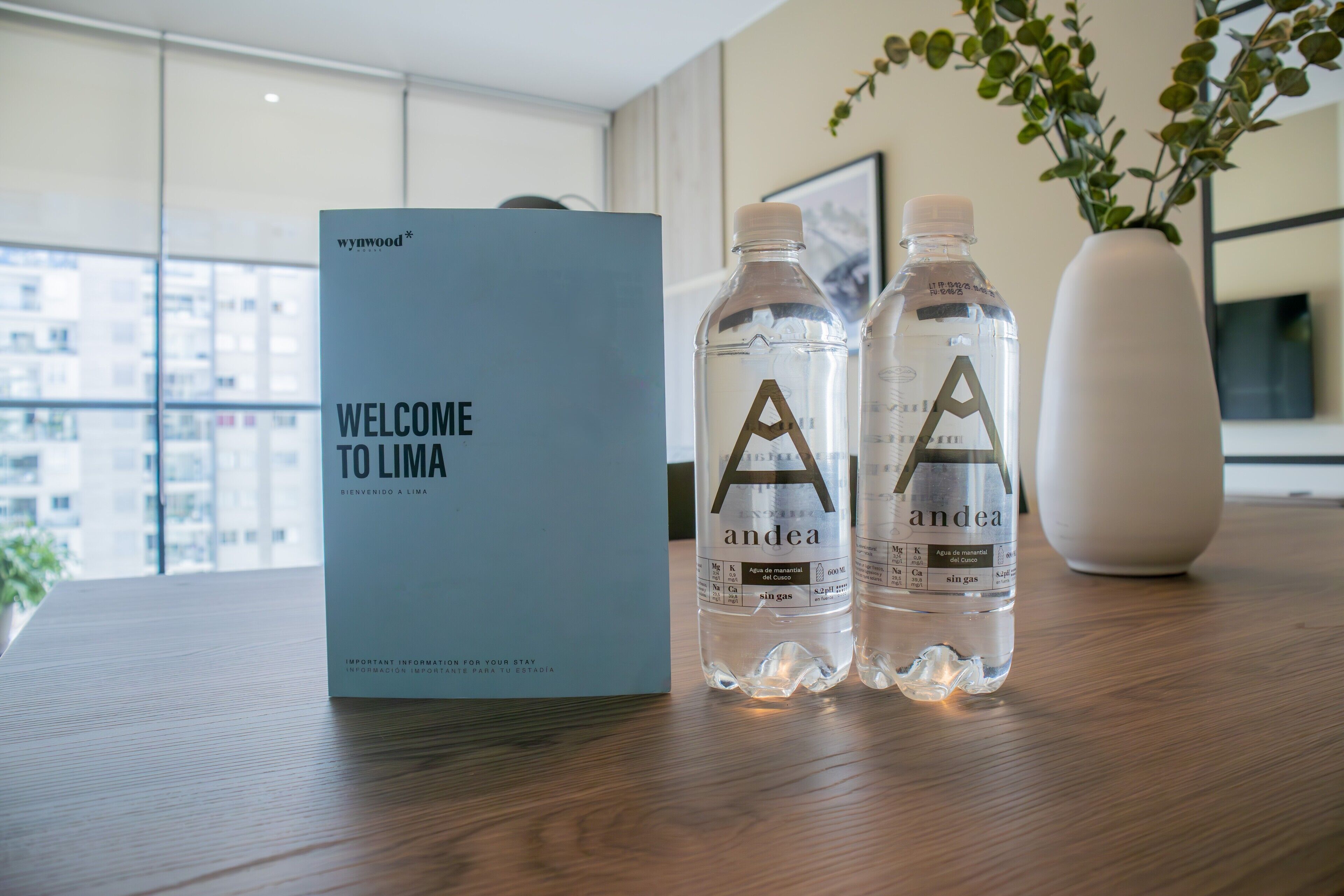Un letrero de bienvenida, dos botellas de agua y un florero sobre una mesa en una habitación moderna con vistas.